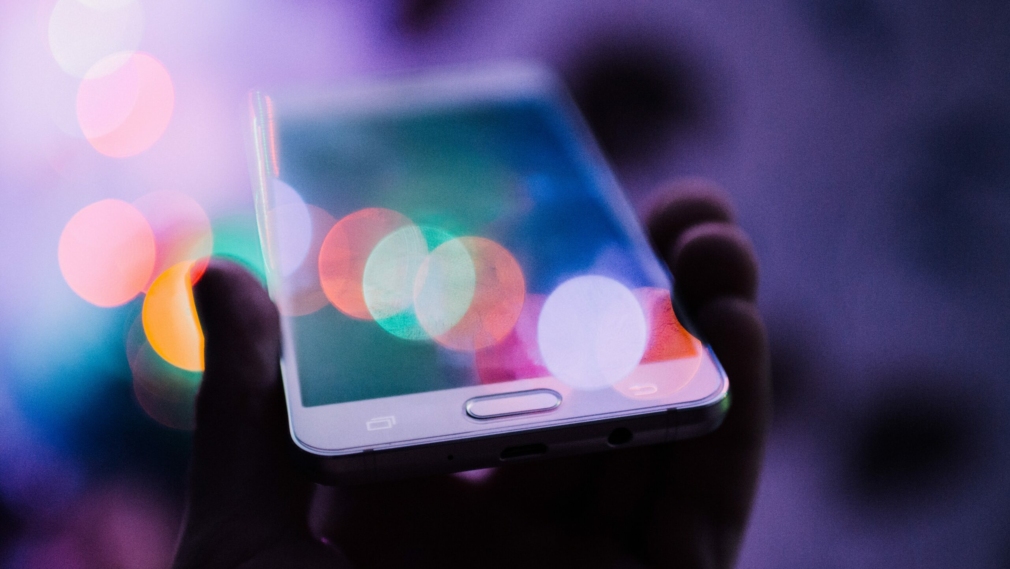 Smartfon trzymany w dłoni, z kolorowymi odbiciami światła na ekranie.