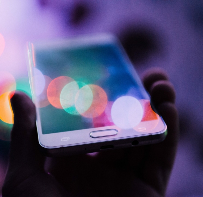 Smartfon trzymany w dłoni, z kolorowymi odbiciami światła na ekranie.