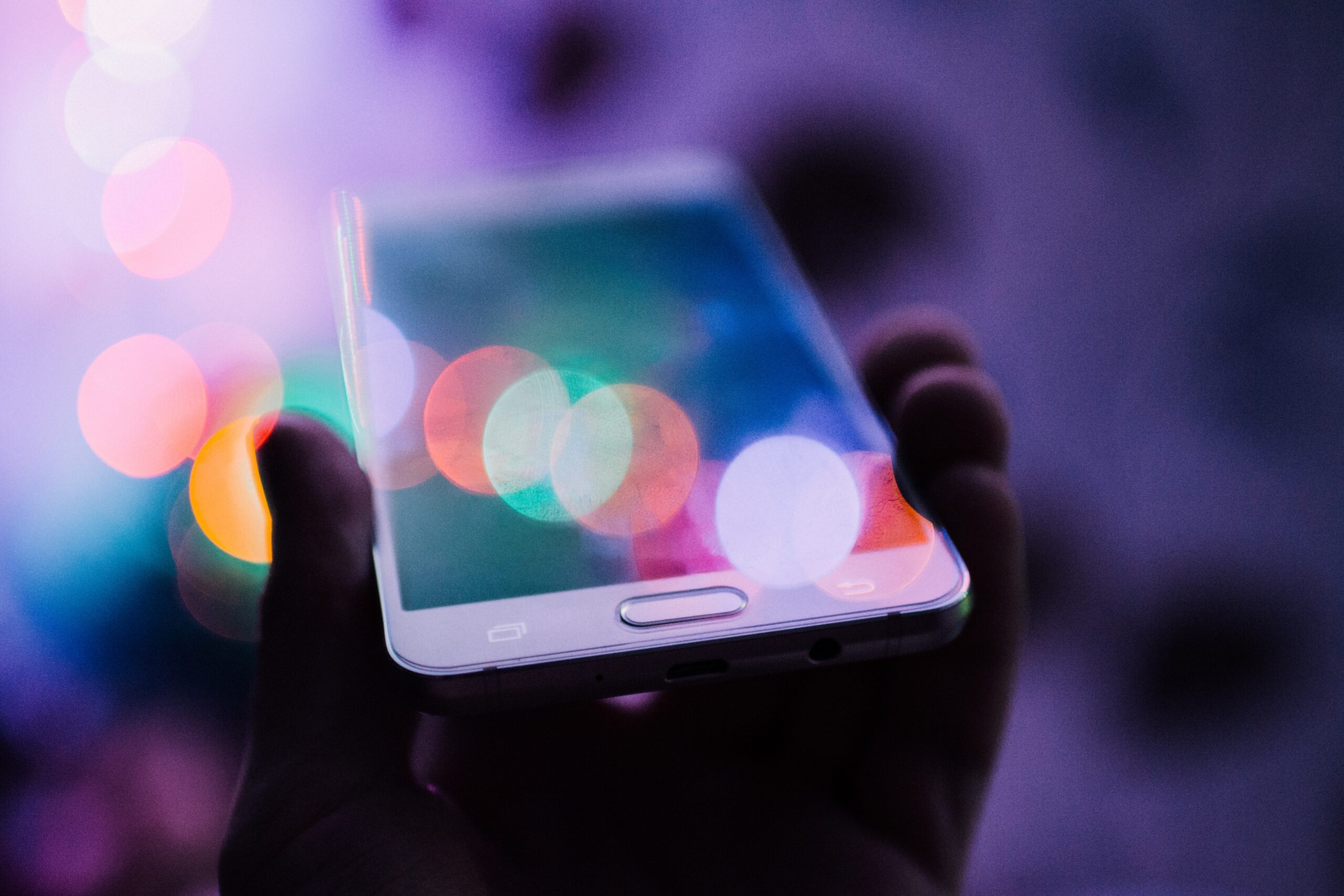 Smartfon trzymany w dłoni, z kolorowymi odbiciami światła na ekranie.