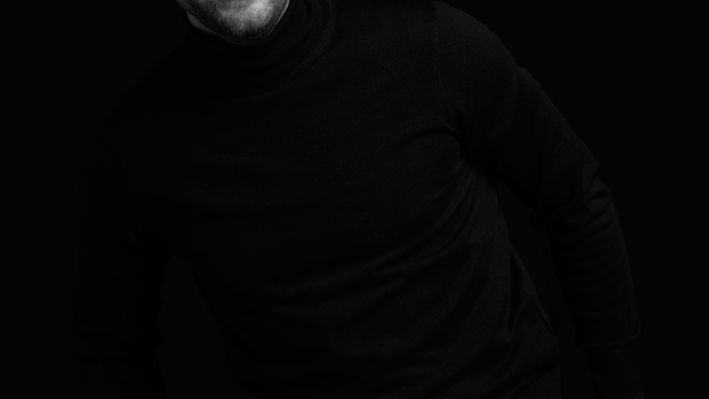 Pawel Makowski pozuje uśmiechnięty w czapce UseCrypt ubrany w okulary czarny golf, zdjęcie jest czarno białe